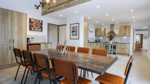 Une cuisine moderne avec des meubles en bois, un coin repas doté d’une grande table et de chaises, et un îlot de cuisine avec un évier et un plan de travail.