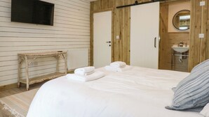 Une chambre à coucher comprenant un lit, une table de chevet, un radiateur, une armoire en bois, et une salle de bain avec un lavabo et un miroir.