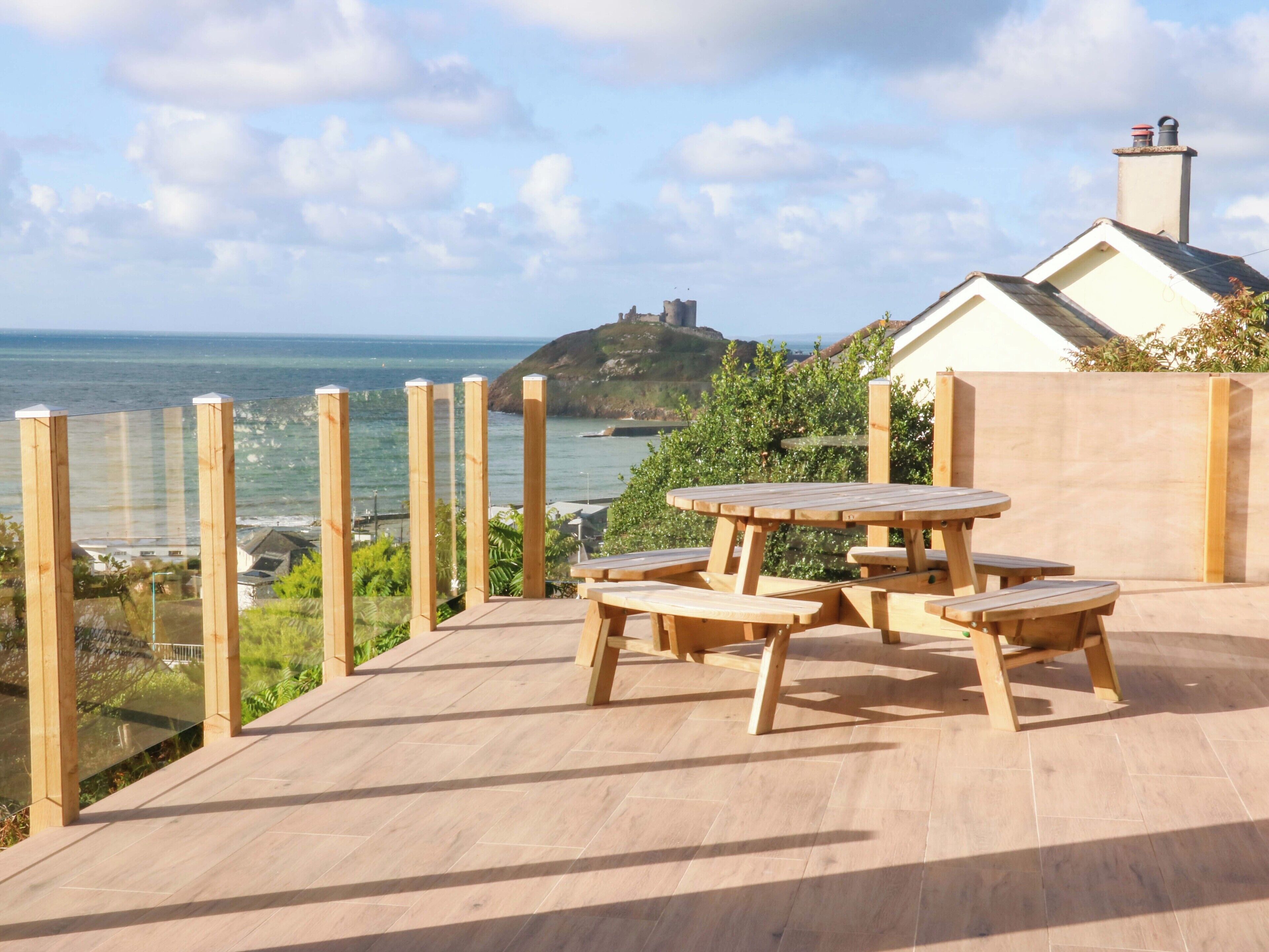 Um deck de madeira com mesa para piquenique e bancos, com vista para o mar.
