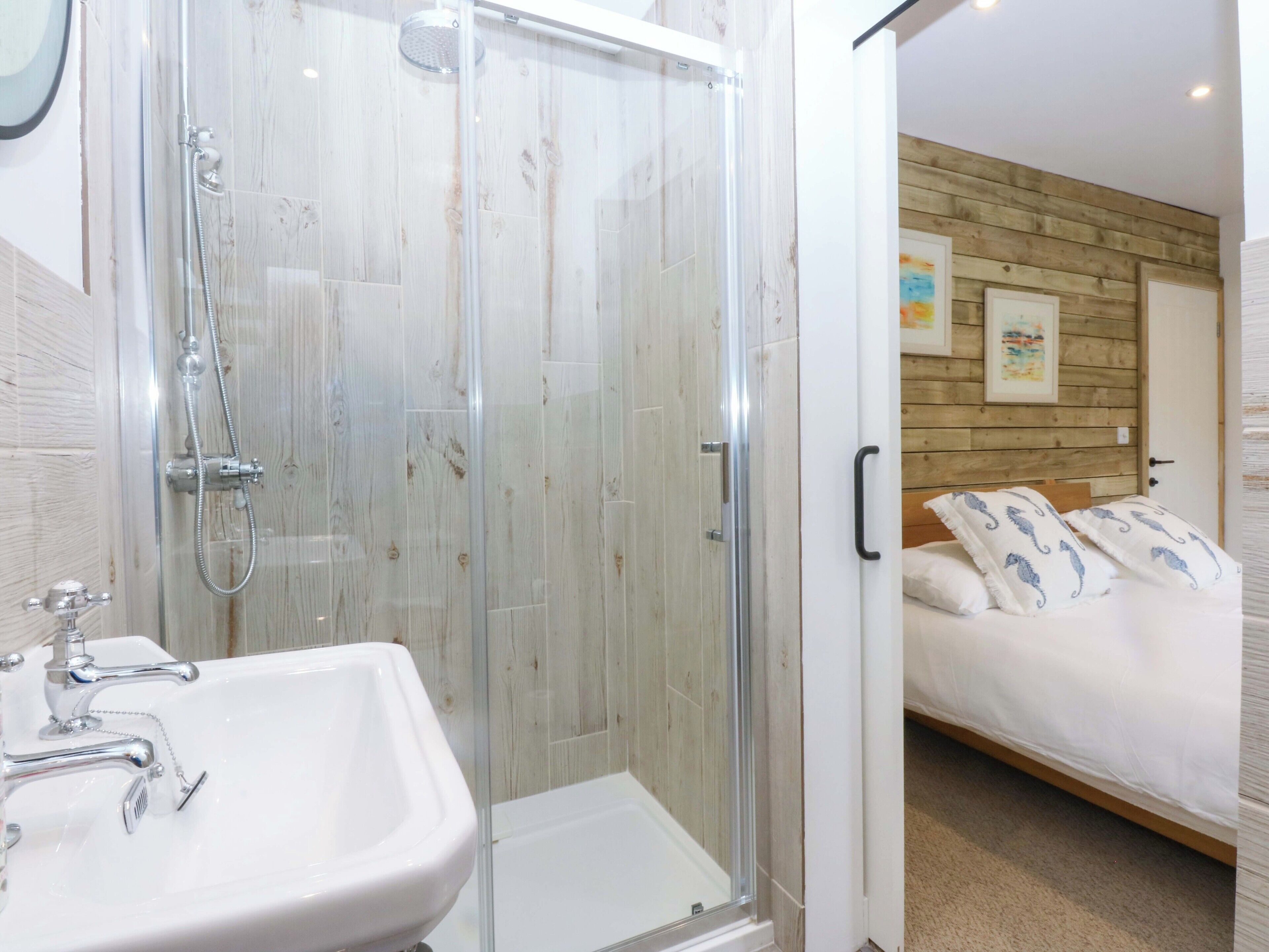 Un bagno con doccia vetrata, lavandino bianco e parete in legno.