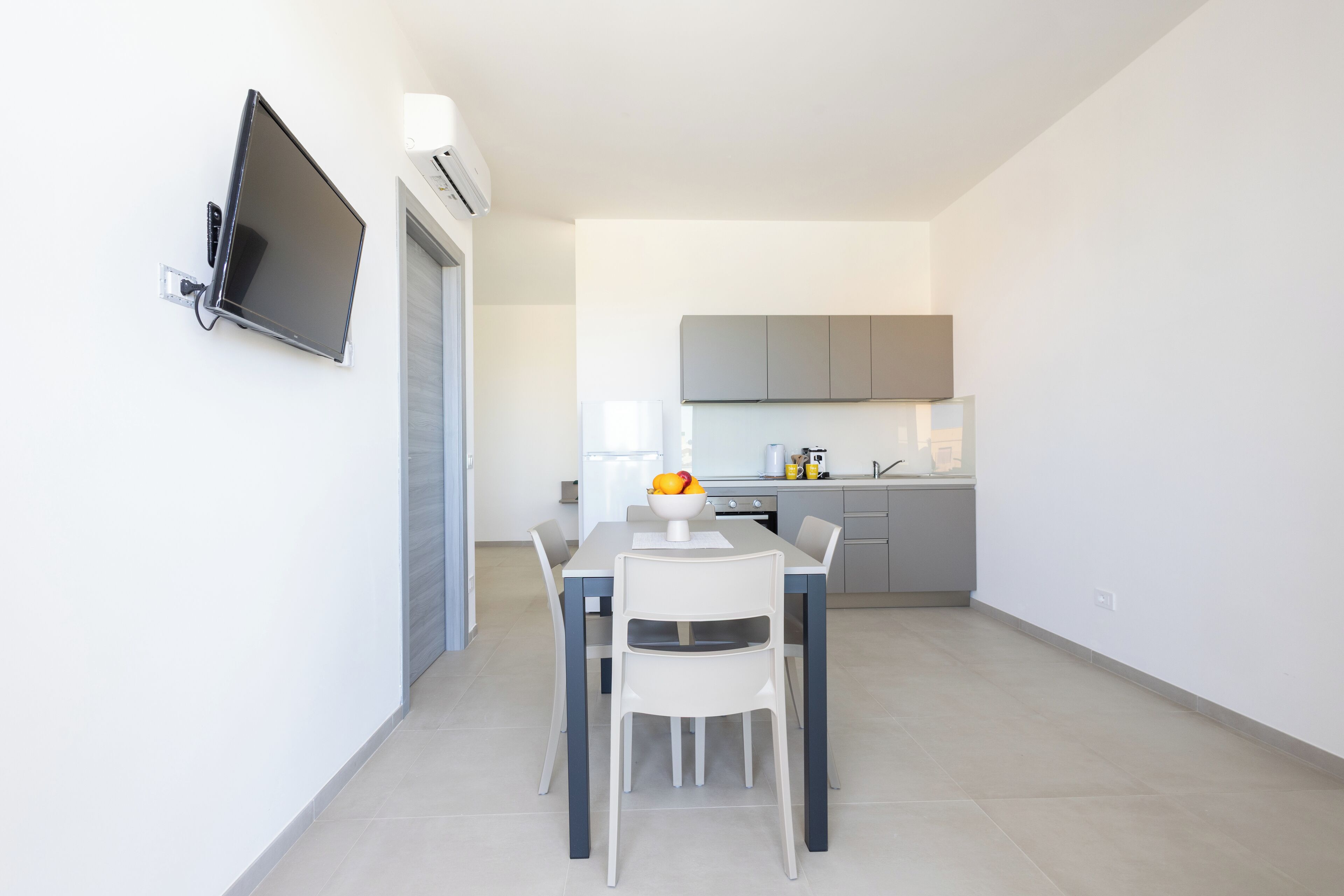A modern kitchen with grey cabinets, a white countertop, and a dining area with a white table and chairs.