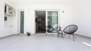 A modern apartment with a balcony, two black wireframe chairs, a small table, and a potted plant.