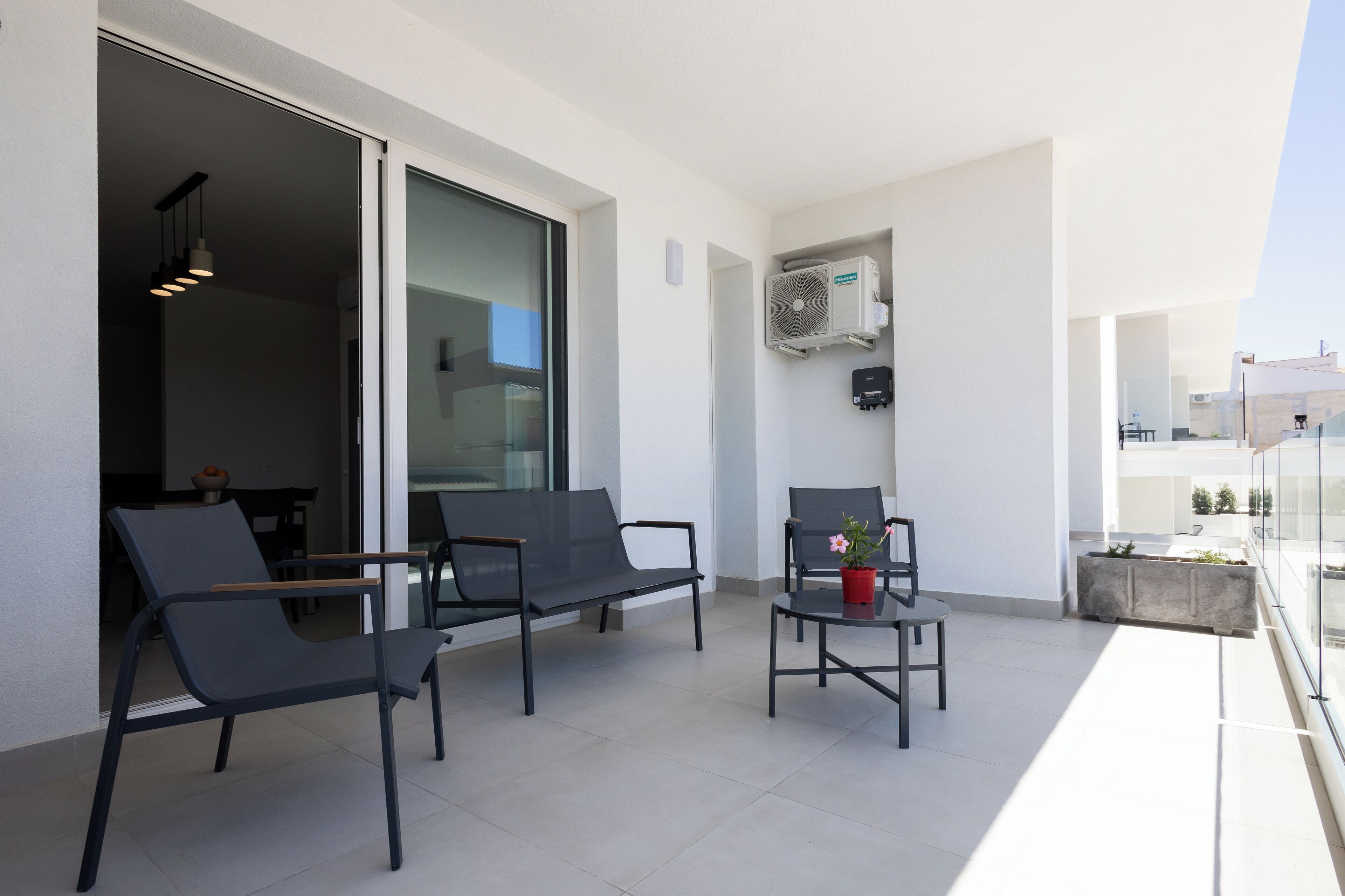 A modern balcony with two black chairs, a small table, and a potted plant.