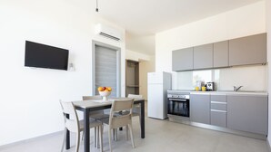 Una cocina moderna con armarios grises, horno empotrado y comedor con mesa y sillas.