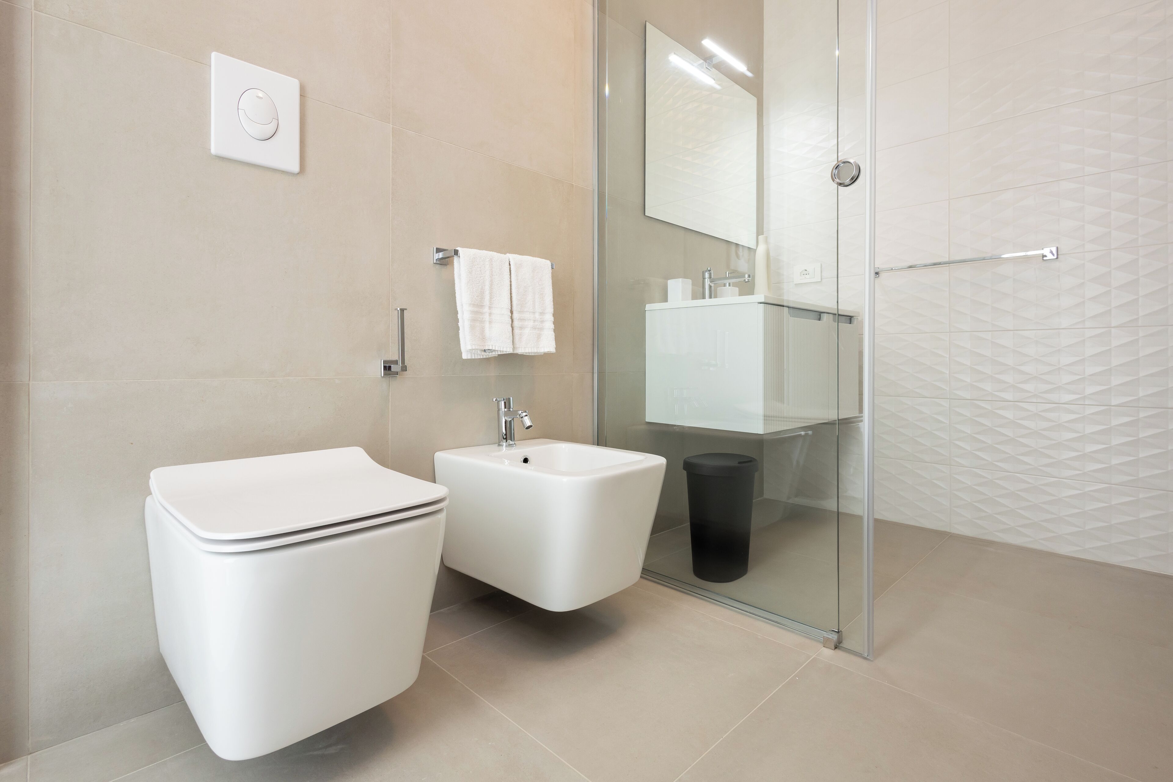 A modern bathroom with a toilet, bidet, and glass shower enclosure.