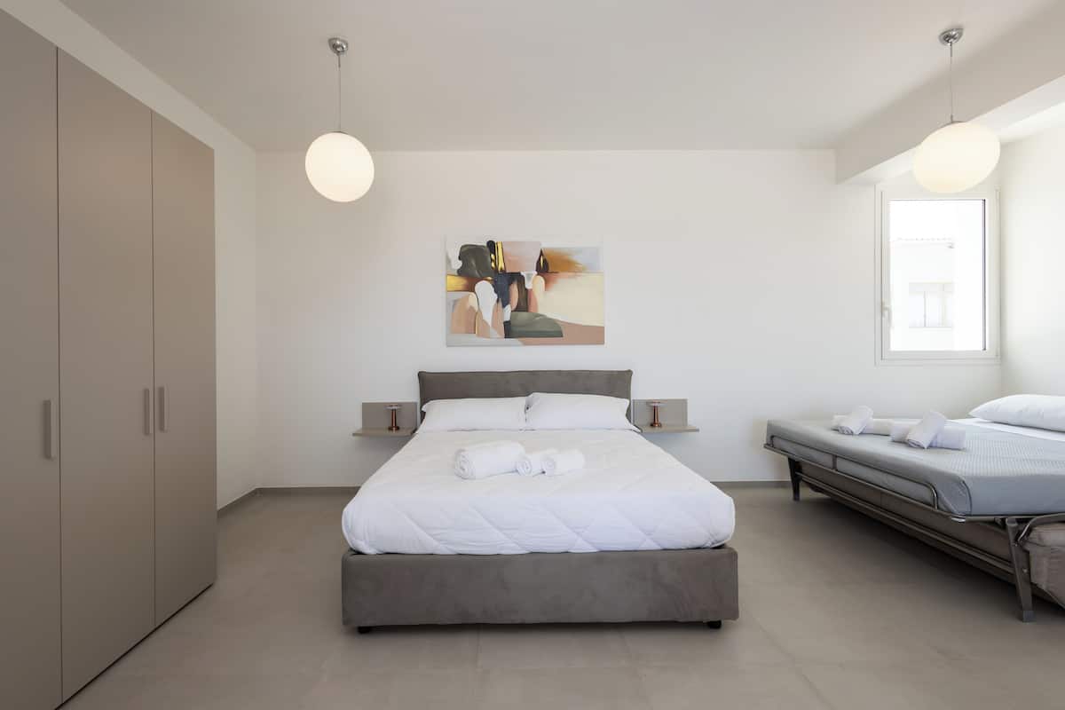 Ein modernes Schlafzimmer mit einem großen Bett, einem kleineren Bett, einem Kleiderschrank und einem Bild an der Wand.
