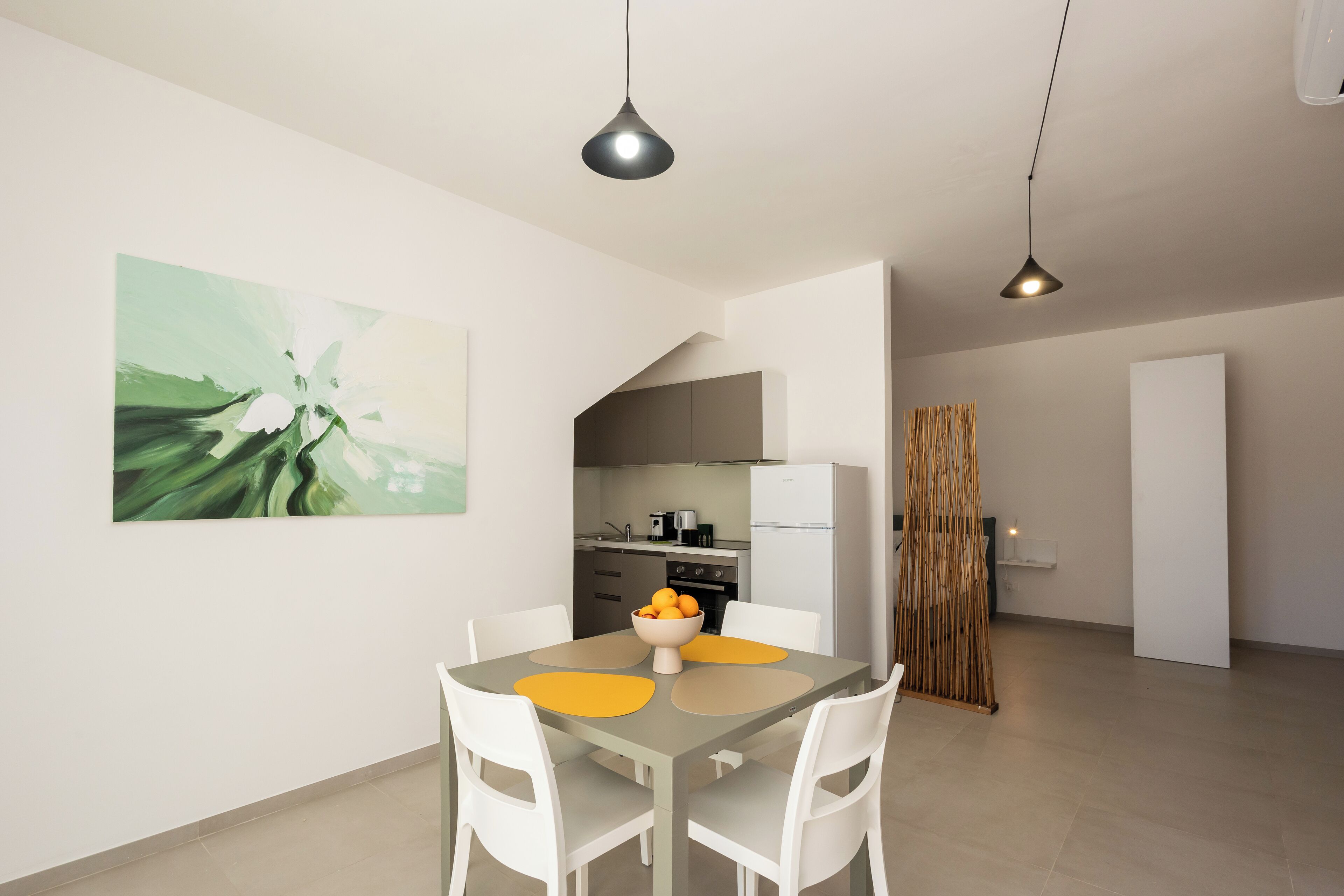 A modern kitchen with white cabinets, a dining area with a table and chairs, and a large abstract painting on the wall.