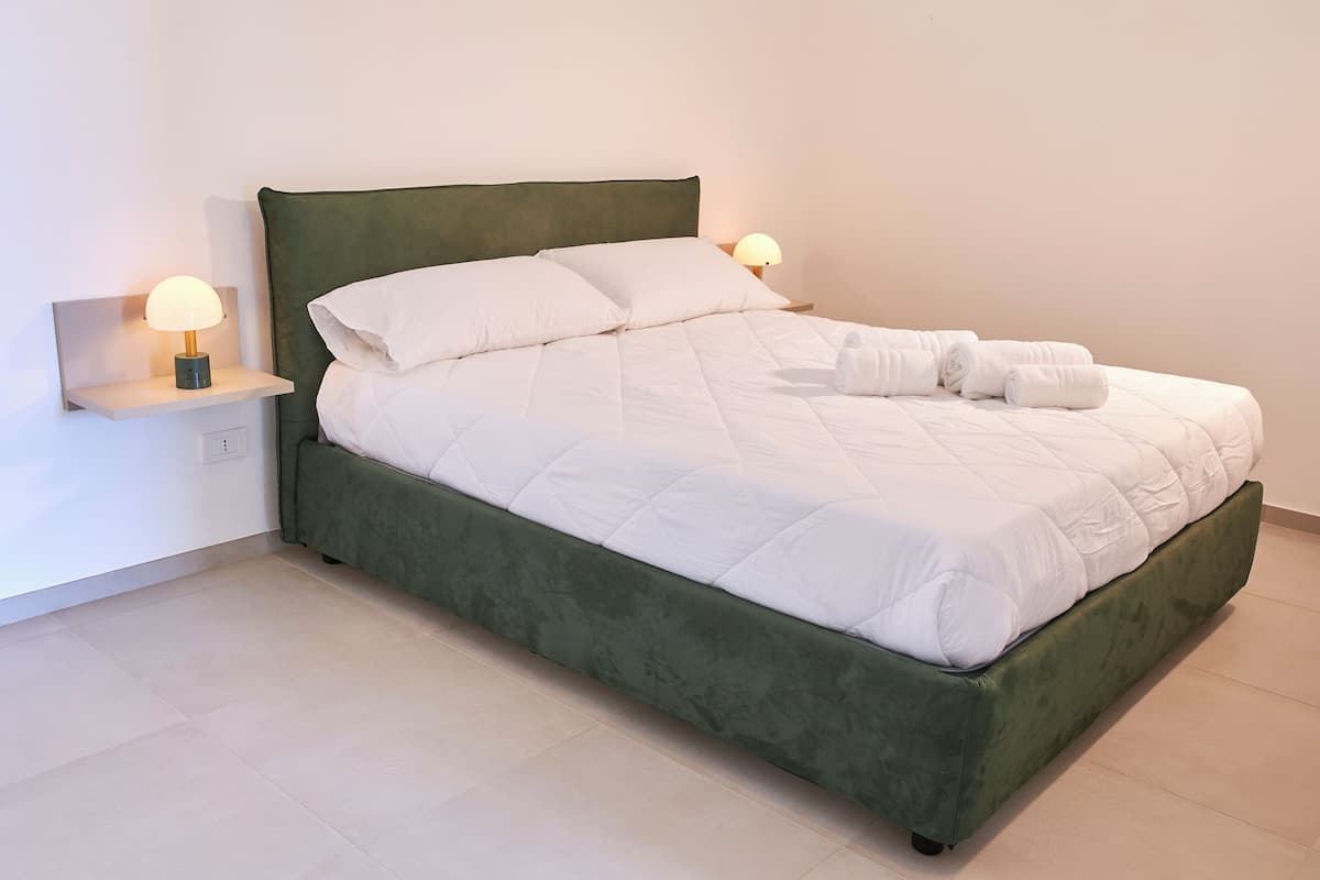 Ein ordentlich bezogenes Bett mit weißer Bettwäsche, zwei Nachttischlampen und einem grünen Kopfteil.
