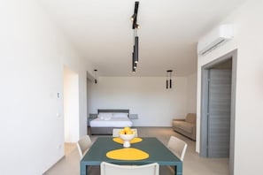 A modern hotel room with a dining table, a bed, a sofa, and a built-in air conditioning unit.