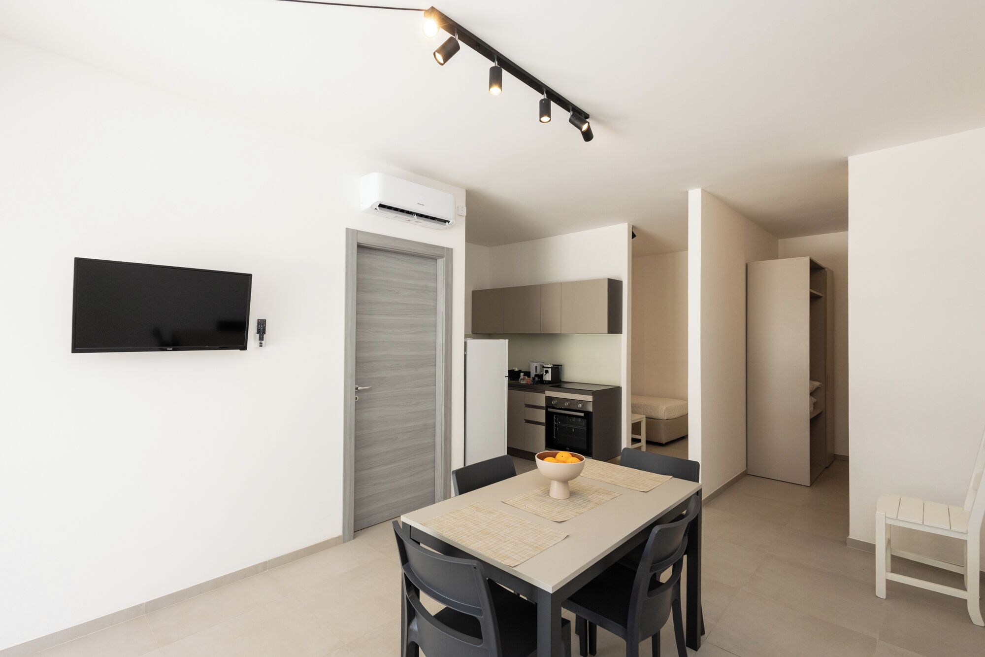 A modern kitchen with a built-in oven, a dining table with chairs, and a TV mounted on the wall.
