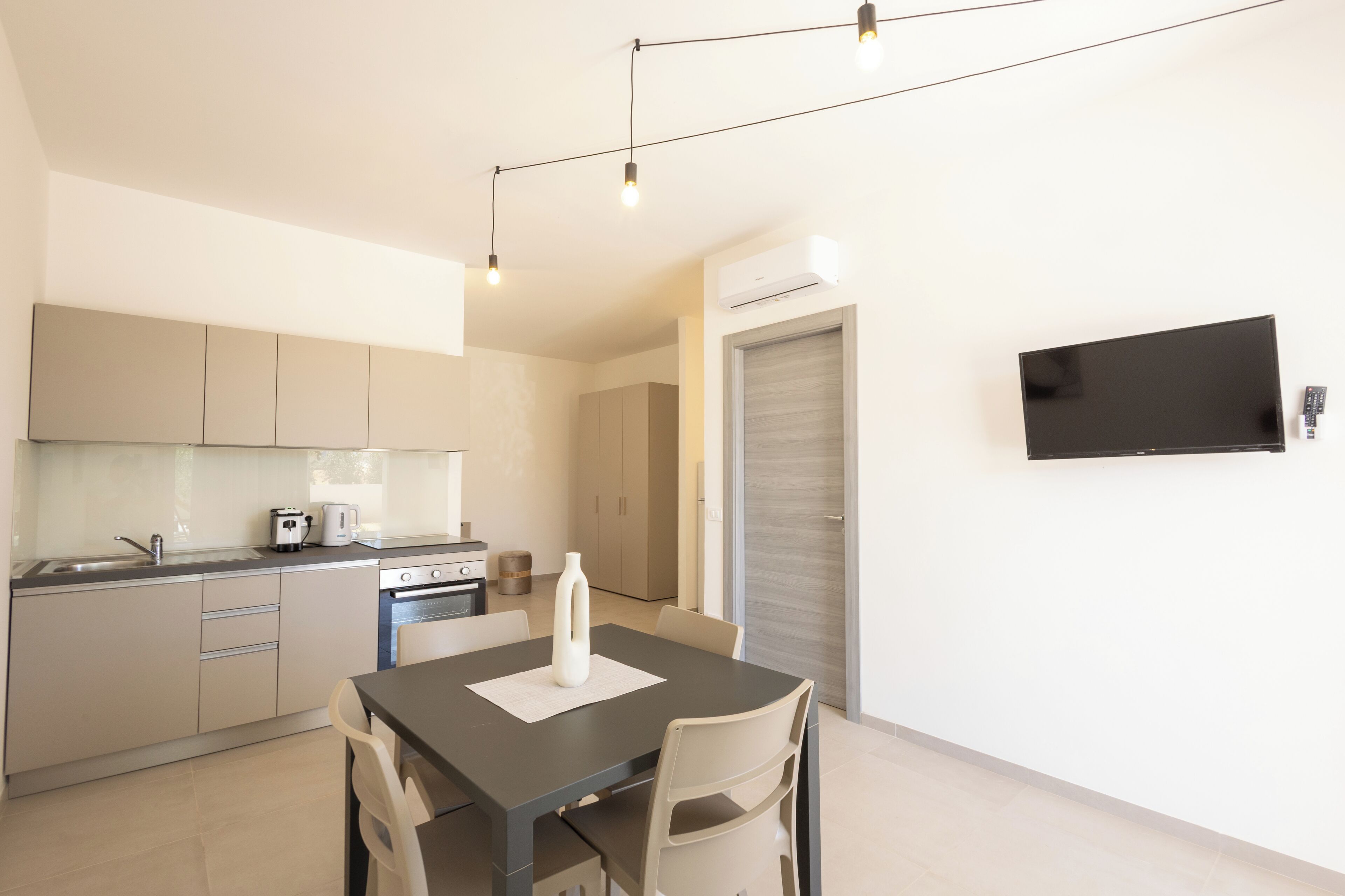 Cozinha moderna com área de refeições, TV de tela plana na parede e armário com porta deslizante.