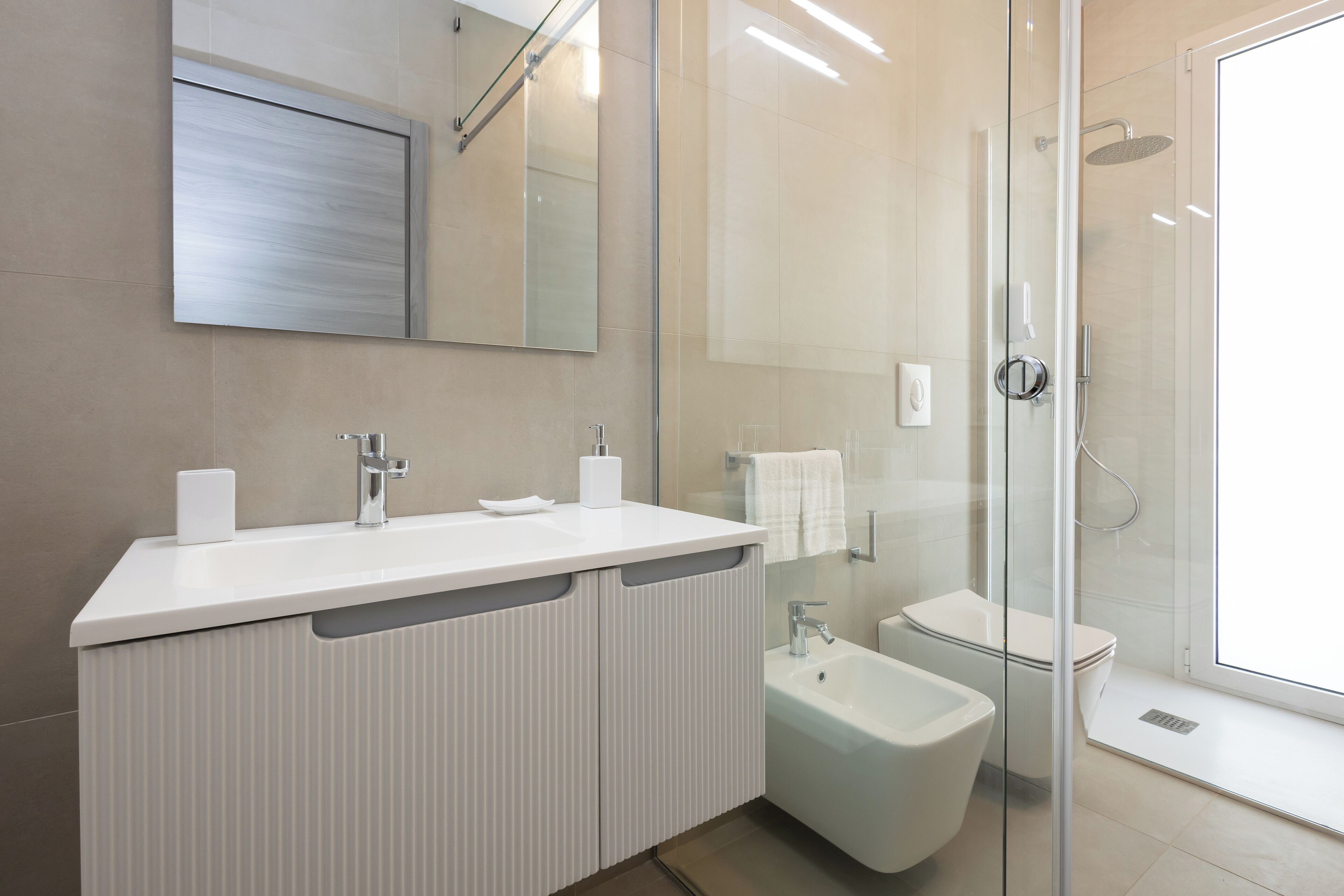 A modern bathroom with a white vanity, a bidet, and a glass-enclosed shower.