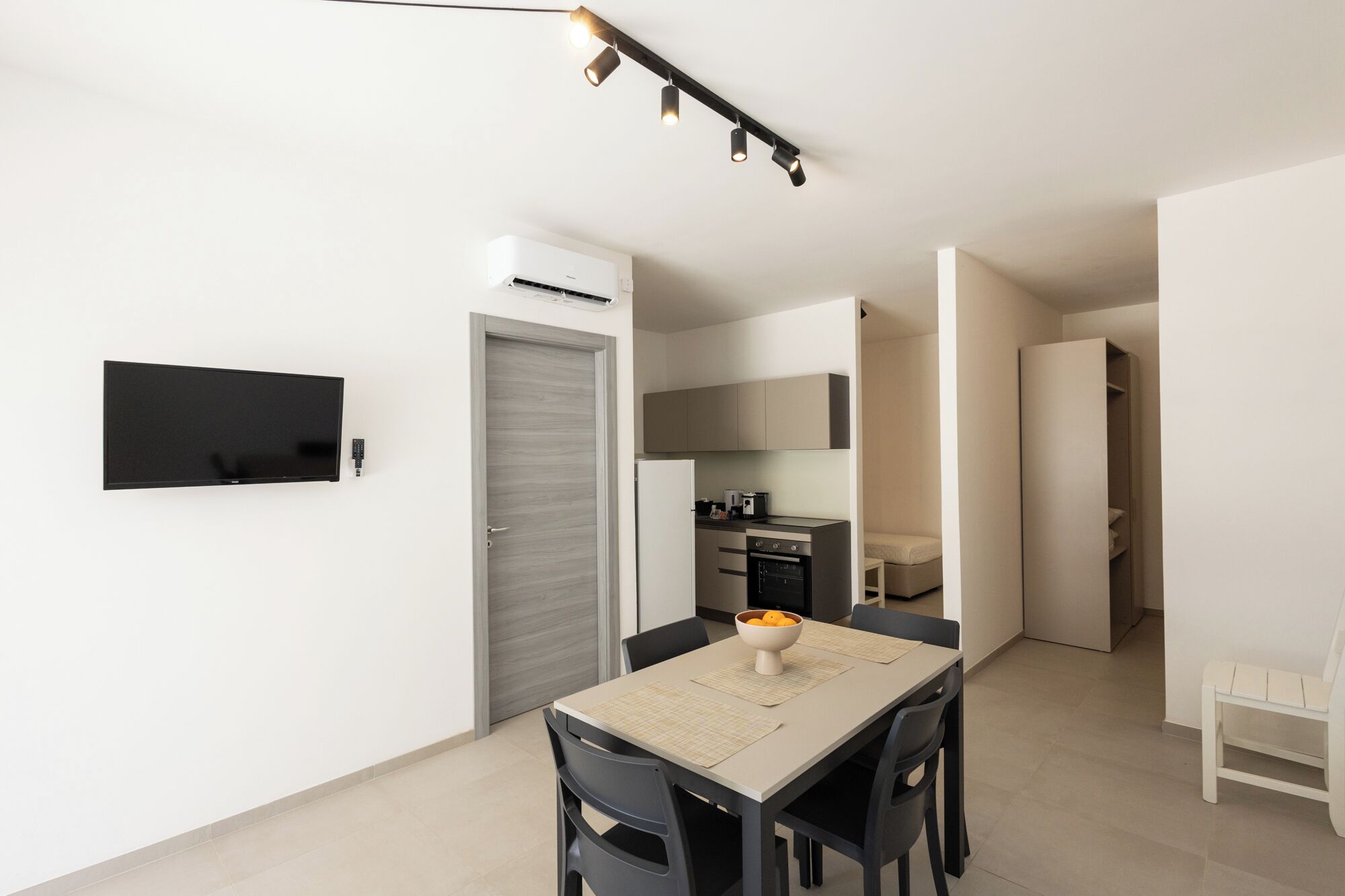 Una cocina moderna con electrodomésticos integrados, una zona de comedor con mesa y sillas, y un televisor de pantalla plana montado en la pared.