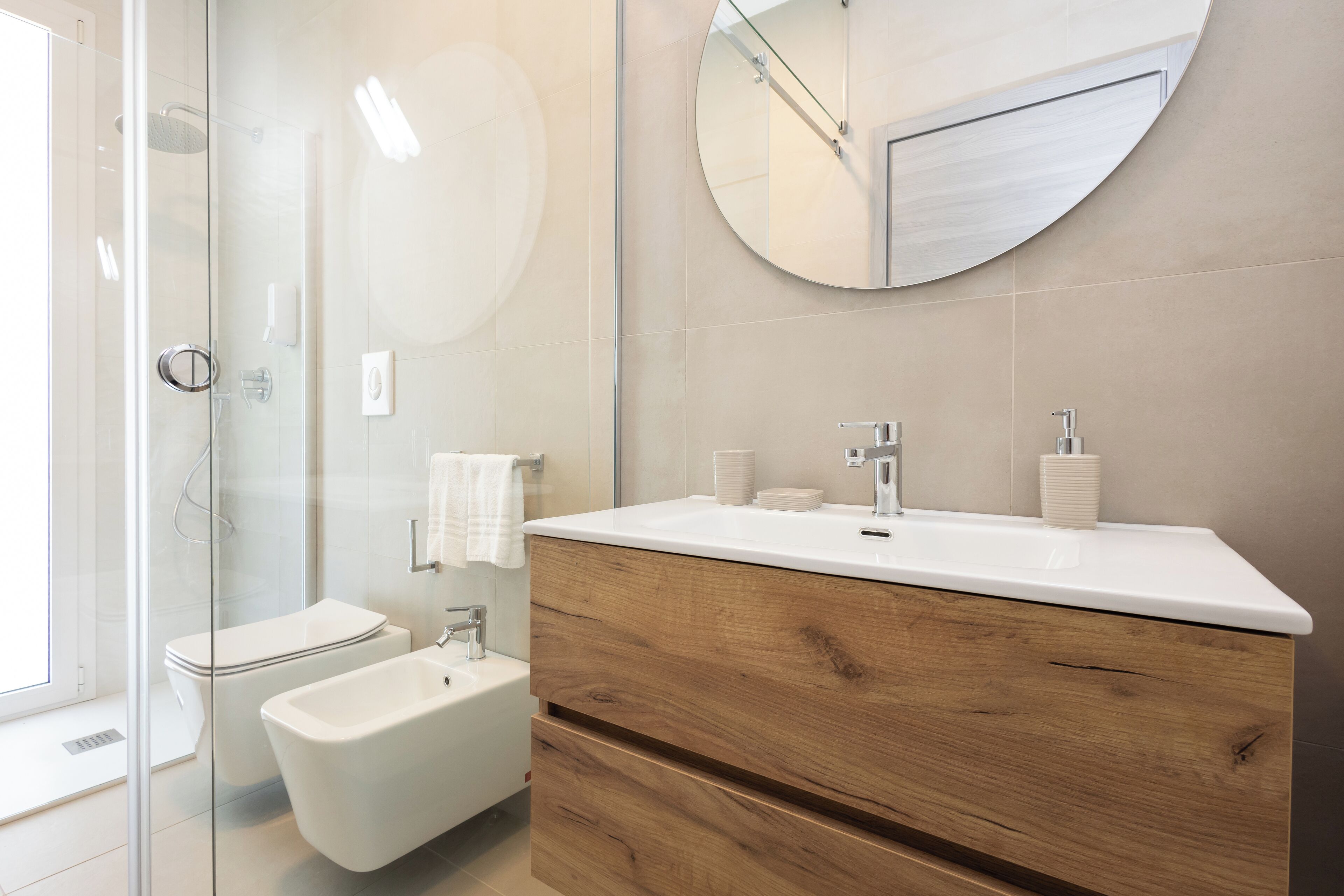 Une salle de bain moderne dotée d’une douche à parois de verre, d’un bidet, d’un meuble-lavabo en bois avec un miroir et de toilettes.