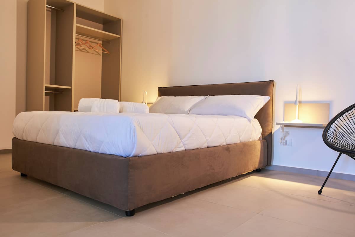 Ein modernes Schlafzimmer mit einem großen Bett, integriertem Kleiderschrank, Nachttisch mit Lampe und einem Sessel.