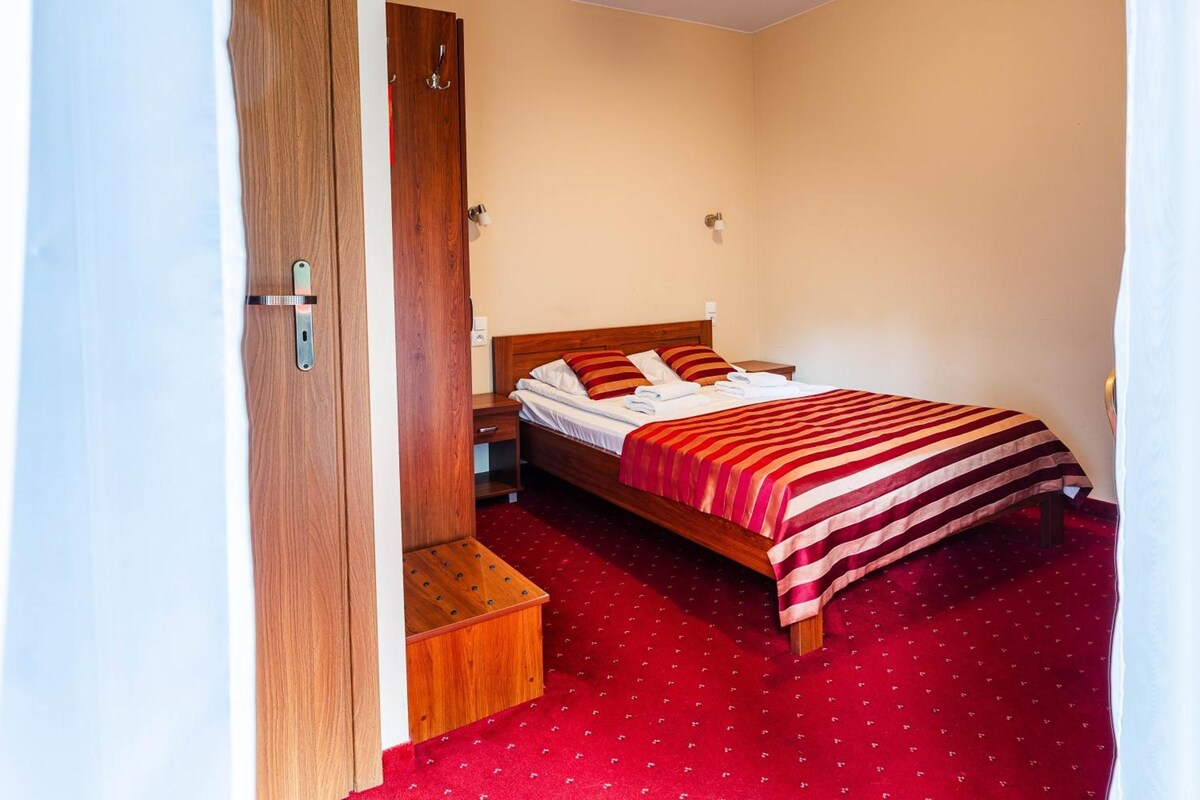 A bedroom with a wooden bed, a red carpet, a wooden nightstand, and a wooden wardrobe.