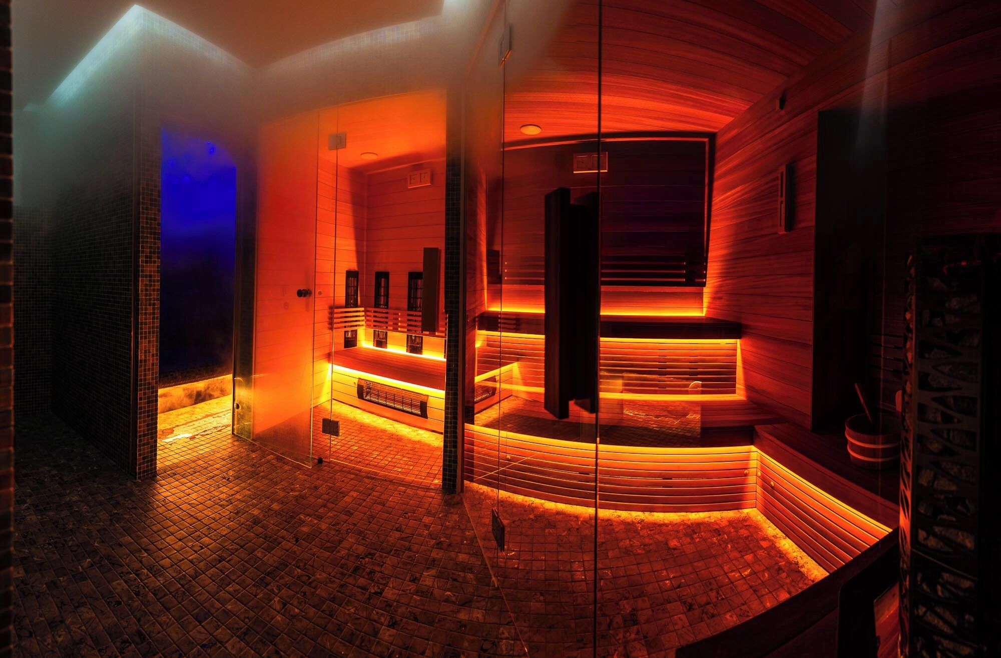 A sauna with a curved wooden interior, a tiled floor, and a glass partition.