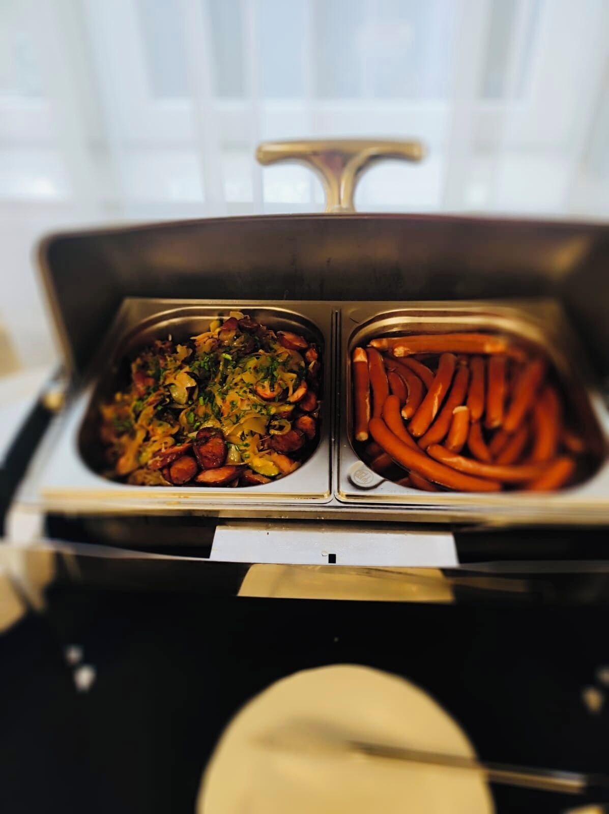 Ein Buffet mit zwei Speisenplatten: eine mit einem Mischgericht und die andere mit Würstchen.