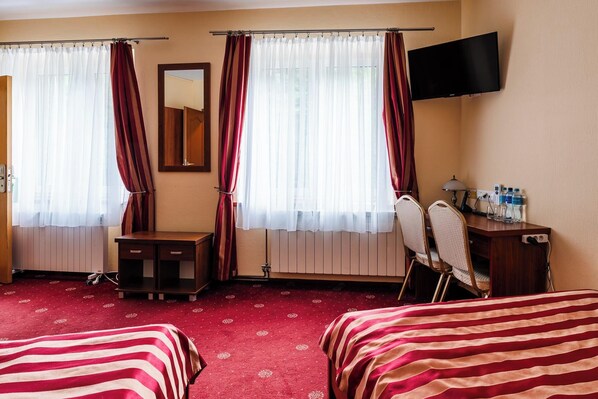 Une chambre d’hôtel avec deux lits, un bureau, une chaise, une télévision et une fenêtre avec des rideaux.