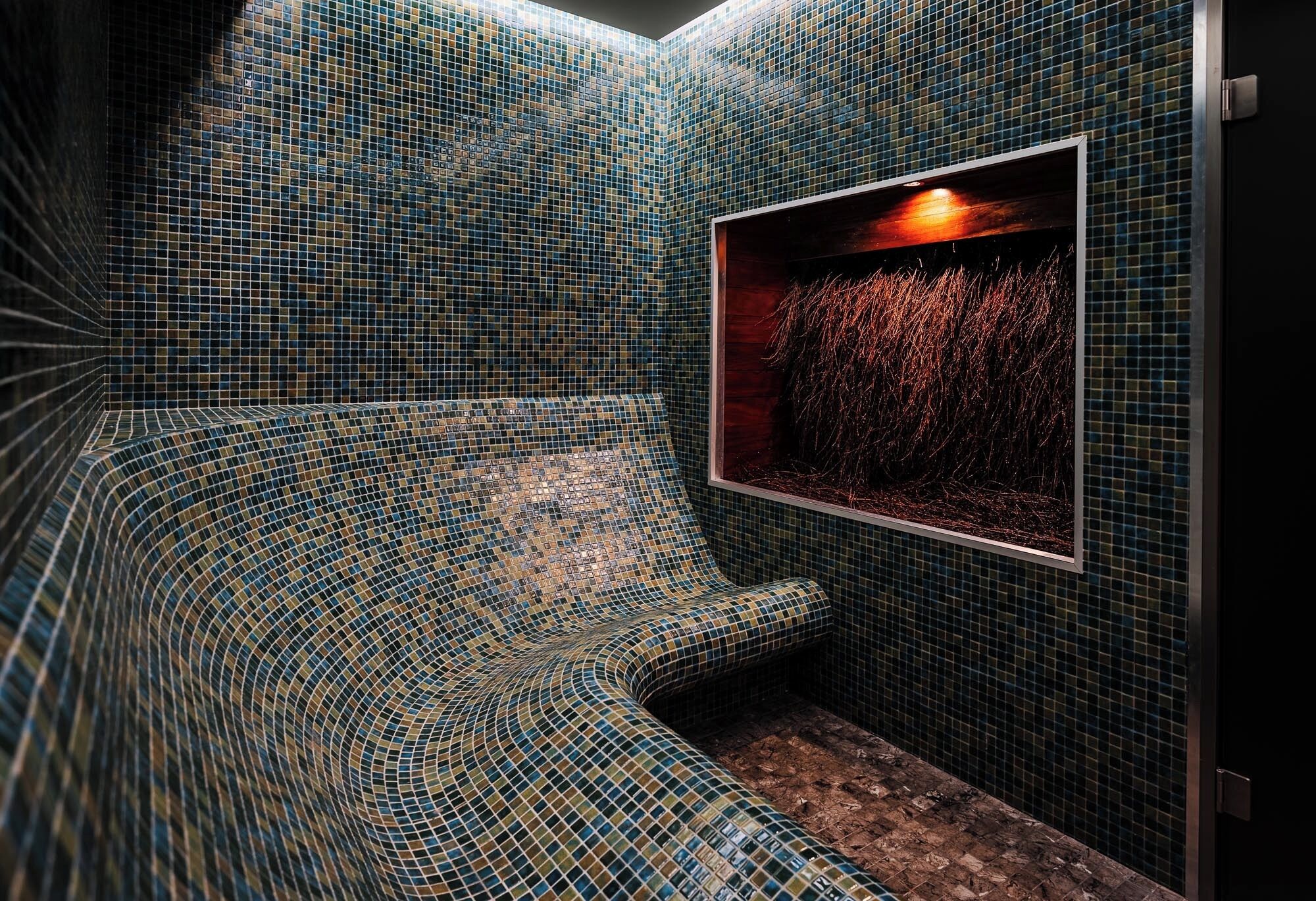 Une salle de bain aux murs recouverts de mosaïques et ornée d’un tableau représentant un coucher de soleil.
