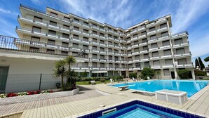 A multi-story hotel with a swimming pool, outdoor seating, and a landscaped garden area.