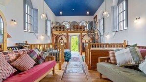 A cozy interior with a wooden staircase leading to a loft, a red sofa, and a green sofa with patterned cushions. - The Zion Chapel, Cinderford - sleeps 4 guests  in 1 bedroom (Soudley, Forest of Dean)