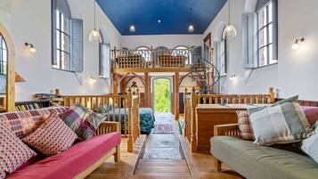 A cozy interior with a wooden staircase leading to a loft, a red sofa, and a green sofa with patterned cushions.
