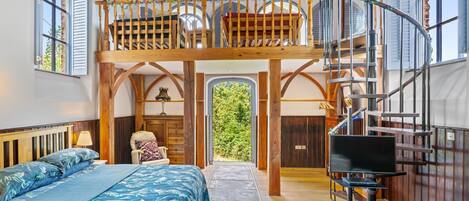 Un dormitorio con cama, una silla, un escritorio, un televisor y una escalera que sube a un altillo.