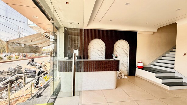 Un espace d’accueil moderne avec un comptoir de réception en marbre, un escalier et une porte vitrée donnant sur l’extérieur.