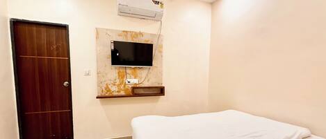A bedroom with a bed, a TV mounted on the wall, a wooden door, and an air conditioning unit.