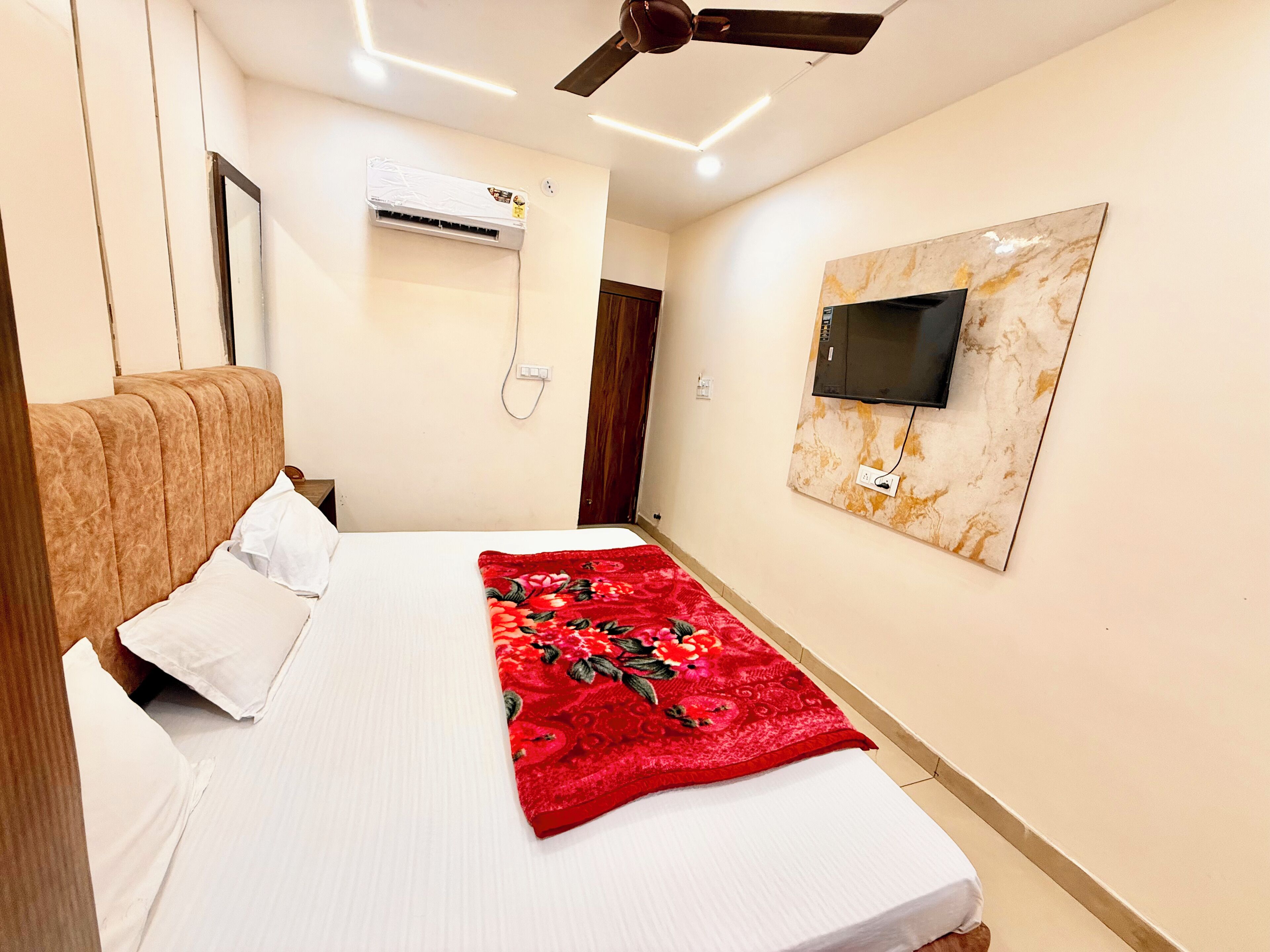 Habitación de hotel con cama, ventilador de techo, unidad de aire acondicionado, televisor montado en la pared y una obra de arte con diseño de mármol.