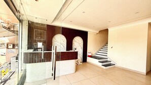 Un espace d’accueil avec une cloison en verre, un comptoir de réception, un mur en marbre et un escalier.
