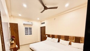 Une chambre d’hôtel avec un grand lit, un ventilateur de plafond, un appareil de climatisation, une fenêtre et une commode en bois.