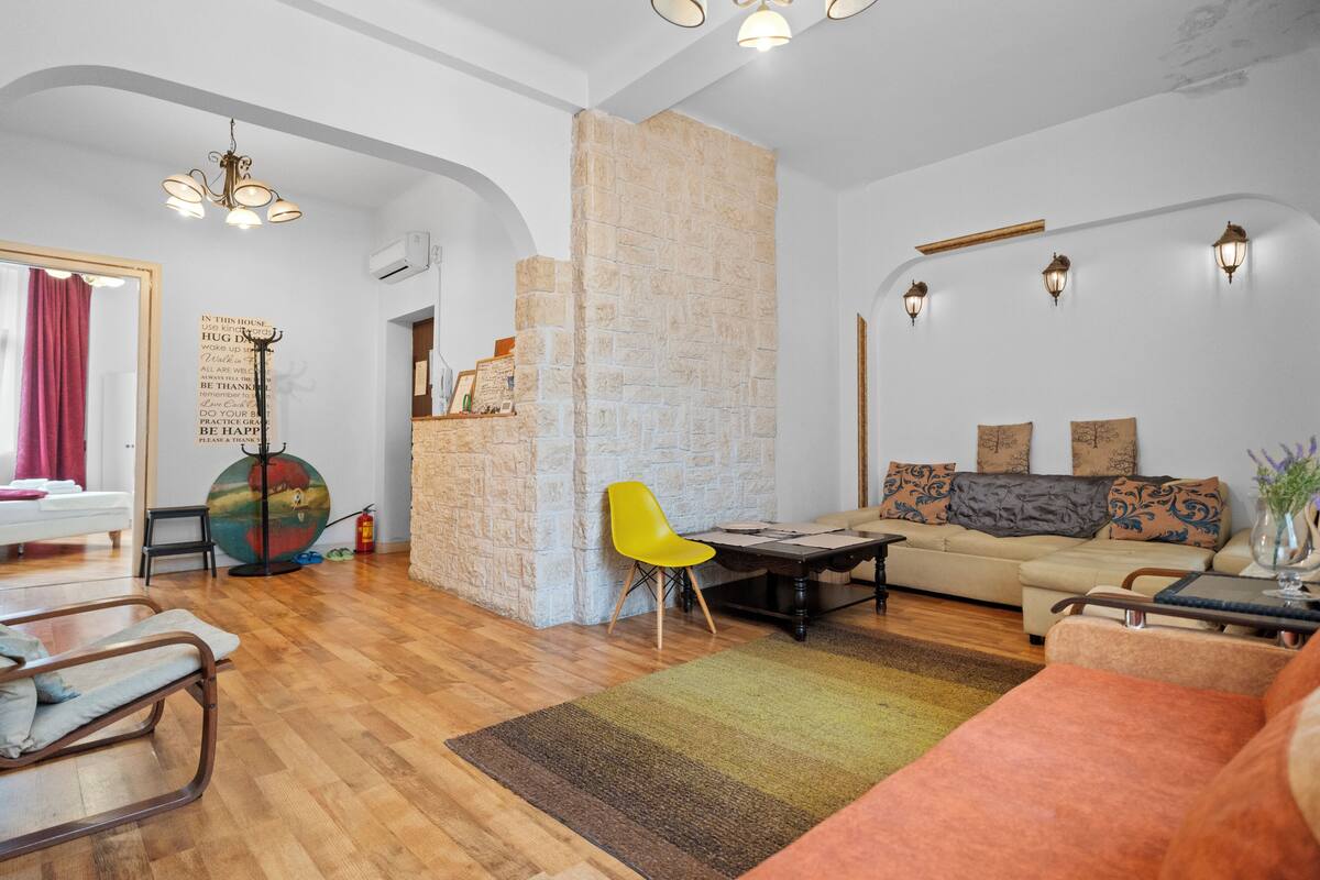 A spacious living area with a wooden floor, a sofa set, a yellow chair, and a stone accent wall.