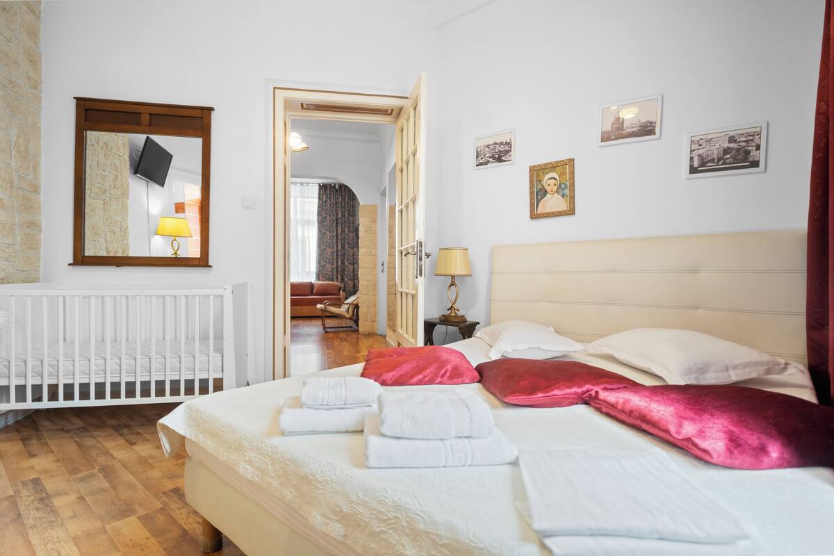 A hotel room with a bed, a white radiator, a mirror, a door leading to another room, and a wall with framed pictures.