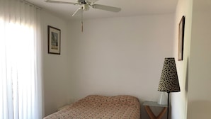 Una camera da letto con un letto, una ventola a soffitto, una lampada e una finestra con persiane.