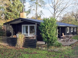 A cabin with a deck, a chimney, and a window overlooking a wooded area. - 4 Star Holiday Home in Hornbaek (Hornbaek)