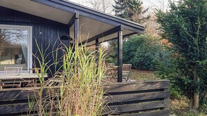 A wooden deck with outdoor furniture, a covered patio area, and surrounding greenery. - 4 Star Holiday Home in Hornbaek (Hornbaek)