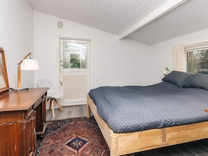 A bedroom with a wooden bed, a desk with a lamp, a chair, and a patterned rug. - 4 Star Holiday Home in Hornbaek (Hornbaek)