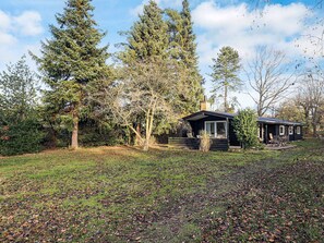 A cabin with a deck, surrounded by trees and a grassy area. - 4 Star Holiday Home in Hornbaek (Hornbaek)