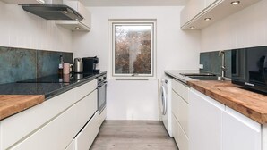 A modern kitchen with white cabinetry, a stainless steel range hood, a window, and a built-in washing machine. - 4 Star Holiday Home in Hornbaek (Hornbaek)