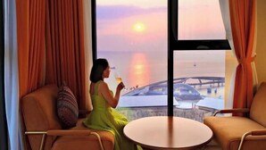 Een kamer met uitzicht op een zonsondergang boven het water, een tafel en twee stoelen.