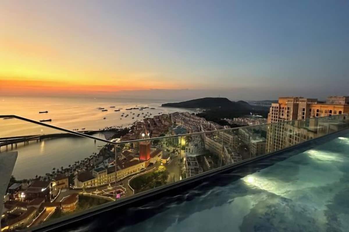 Une vue panoramique d’une ville côtière au coucher du soleil, avec un pont, des bateaux et des bâtiments.