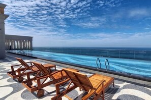 A poolside area with lounge chairs and a view of the ocean.