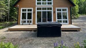 A two-story wooden house with large windows, a deck, and a gravel driveway.