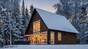 A cabin with a sloped roof, large windows, and a covered patio area.