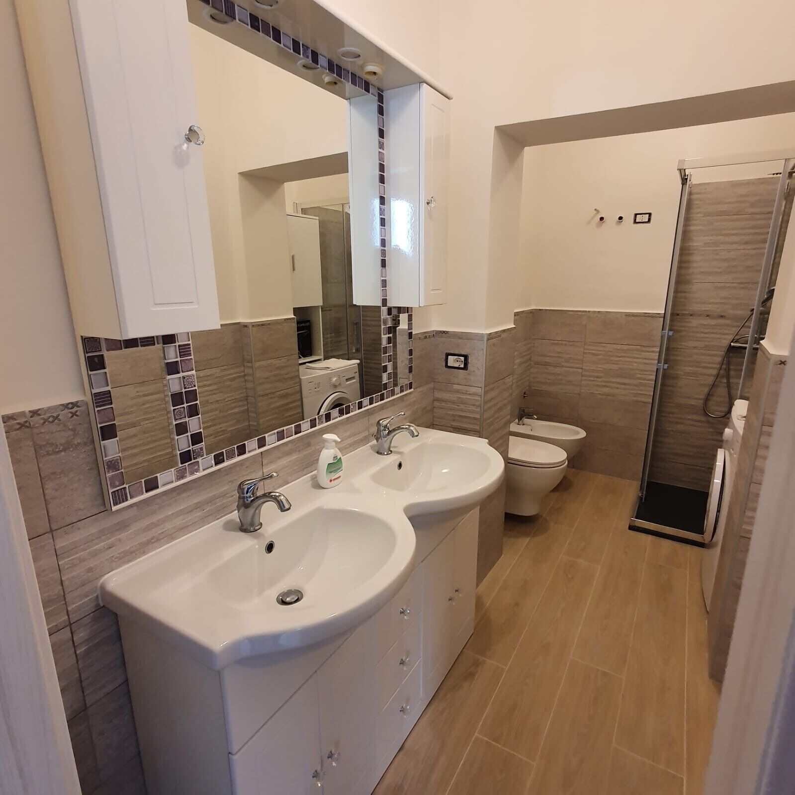 Un baño moderno con dos lavamanos, un espejo, un inodoro y una ducha.