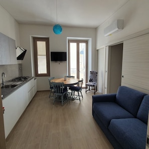 A compact kitchen with a dining area, a sofa, and a TV.