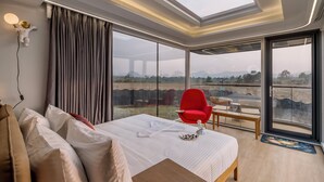 A modern hotel room with a large bed, a red chair, a wooden table, and a large window with a view of the outdoors. - Astrophile (Vada)