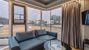 A modern living room with a leather sofa, a glass coffee table, and large windows offering a view of outdoor amenities. - Astrophile (Vada)